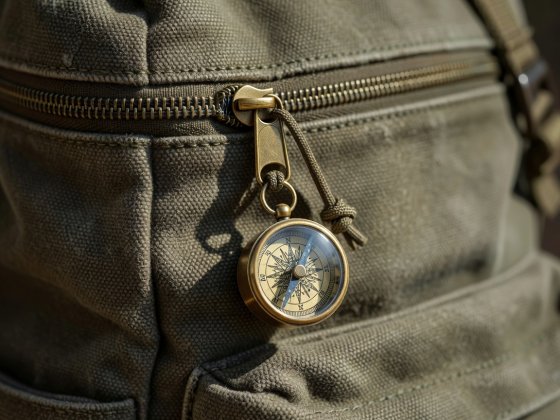 Close-up of a sturdy canvas backpack zipper with a brass mini compass attached to the pull cord
